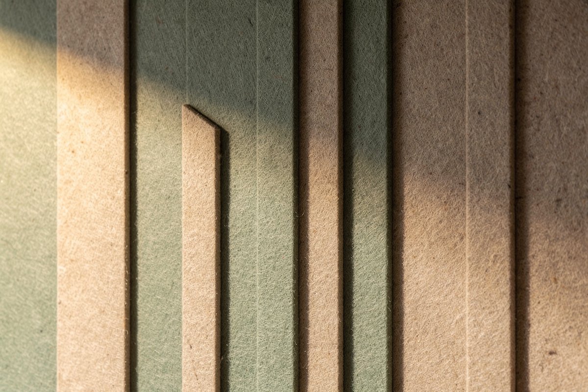 Détail de panneaux acoustiques en feutre aux tons sauge et avoine, composition murale géométrique.