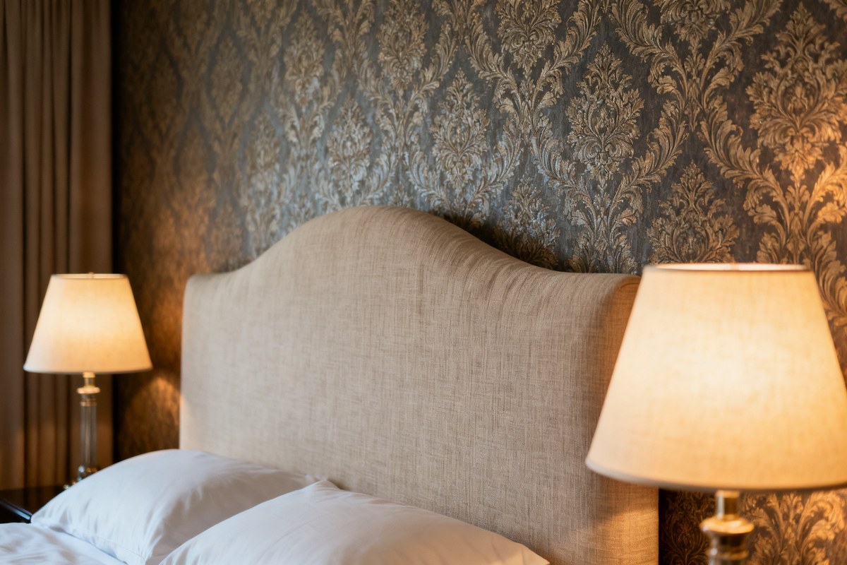 Papier peint à motif damassé derrière une tête de lit en lin clair dans une chambre