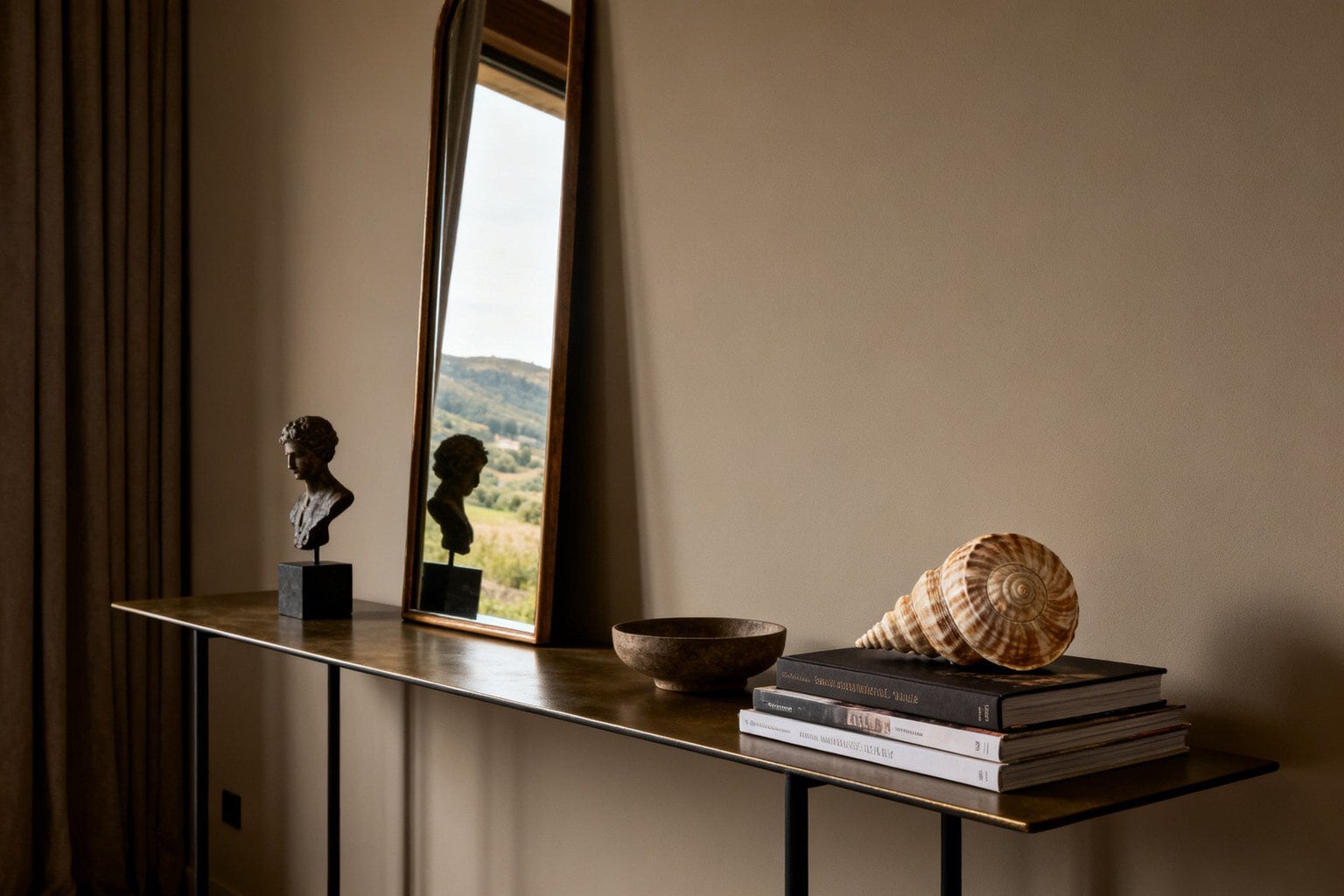 Console fine avec un buste antique, un miroir arqué, un bol et une grande coquille en spirale posée sur des livres