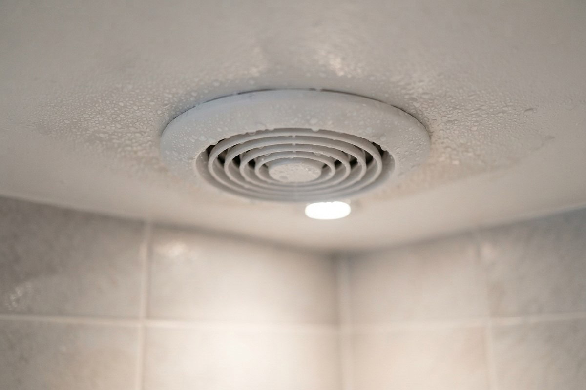 Bouche d'extraction ronde au plafond d'une salle de bains, entourée de gouttes de condensation